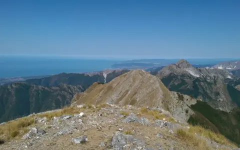 Panoramica mozzafiato dal monte Argegna, con il mare azzurro all'orizzonte e le cime rocciose che si stagliano contro il cielo limpido.