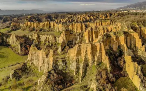 Paesaggio surreale nella provincia di Arezzo, con calanchi dorati che si ergono tra colline verdi e alberi spogli.