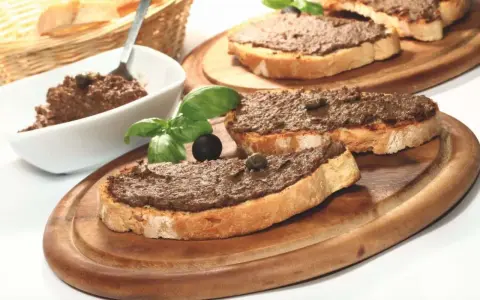 Toasted bread slices topped with dark spread, garnished with basil, olives, and capers.