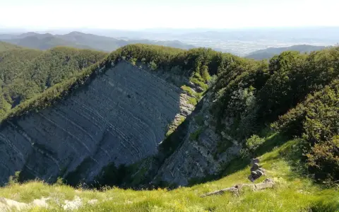 Panoramica mozzafiato sull'Alpe della Luna, con rocce stratificate che si ergono tra boschi rigogliosi e un cielo azzurro.