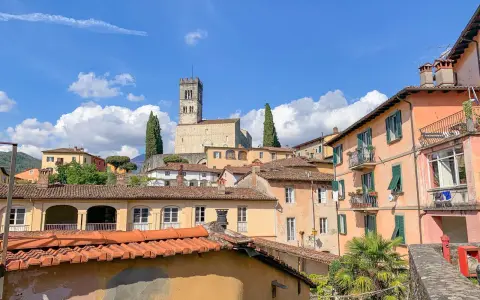 Panoramica di Barga, Lucca, con case colorate e il Duomo in cima alla collina sotto un cielo azzurro con nuvole bianche.