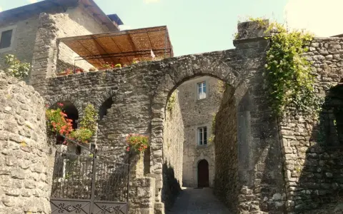 Un vicolo antico a Casola in Lunigiana, con un arco in pietra, mura di sassi e fiori rossi che sbocciano.