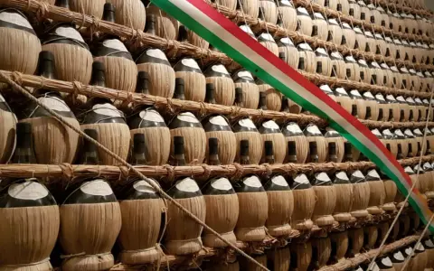 Una grande esposizione di bottiglie di vino impagliate, forse un omaggio alla tradizione della villa poggio reale rufina, con un tricolore italiano che le attraversa.