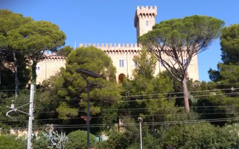 Il Castello Pasquini, con la sua torre imponente, emerge tra alberi verdi e un cielo azzurro.