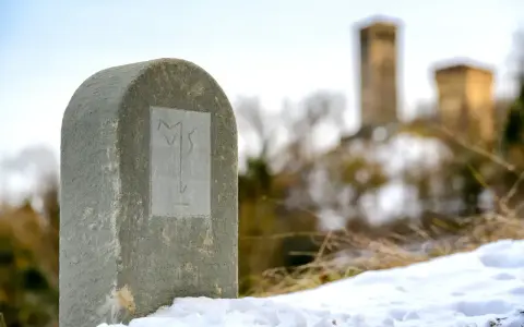 Monumento in pietra con simbolo inciso, sulla via Matildica del Volto Santo. In lontananza, castelli innevati.