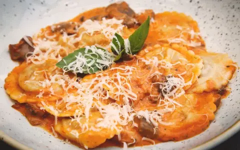 Tordelli versiliesi in un piatto bianco, conditi con sugo rosso, funghi, parmigiano grattugiato e basilico fresco.