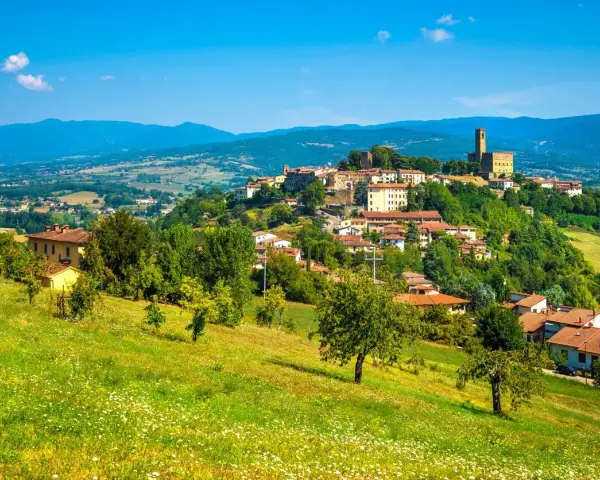 Borgo medievale in collina, un gioiello del Casentino cosa vedere. Case con tetti rossi, verde rigoglioso e un cielo azzurro intenso.