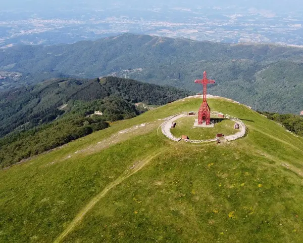 La croce del Pratomagno domina un paesaggio verdeggiante, con montagne boscose e una città in lontananza.