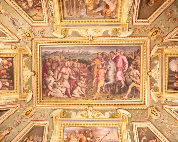 Soffitto affrescato con scene storiche e figure mitologiche, un capolavoro che evoca la grandezza del **Palazzo Vecchio**.