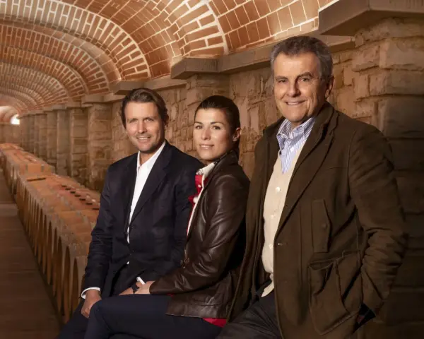 Tre persone sorridono nella cantina della Tenuta Il Borro, circondati da botti di vino e un soffitto a volta in mattoni.