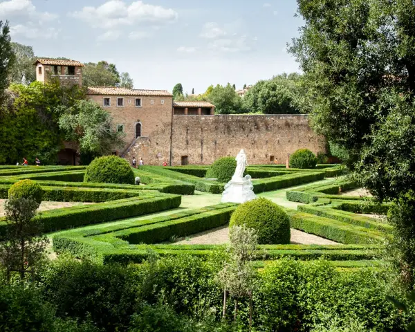Giardini geometrici a San Quirico d'Orcia con statua bianca e edifici storici sullo sfondo.