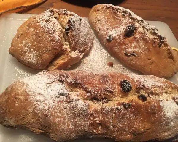 Tre panini aretini dorati, cosparsi di zucchero a velo e uvetta, pronti per essere gustati.