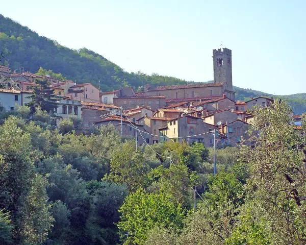 Antica villa basilica con torre campanaria, immersa nel verde di una collina toscana.