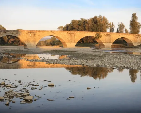 Ponte romanico con archi a tutto sesto, riflesso sull'acqua calma. I Setteponti di Arezzo, un'antica via, abbraccia la campagna toscana.