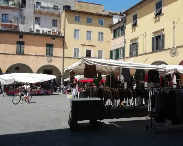 Mercato all'aperto nella piazza delle vettovaglie, con bancarelle di abbigliamento e persone che passeggiano.