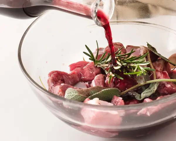Vino rosso versato su cubetti di carne e aromi per macerare cinghiale.