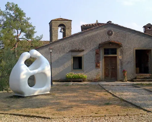 Scultura moderna di due figure abbracciate, simbolo di romena accoglienza, davanti a un edificio con campanile.