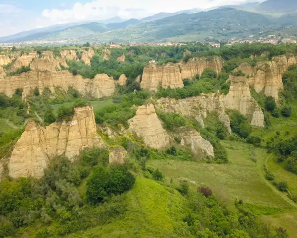 Le suggestive balze del Valdarno, scolpite dal tempo, si ergono tra verdi colline e un borgo in lontananza.