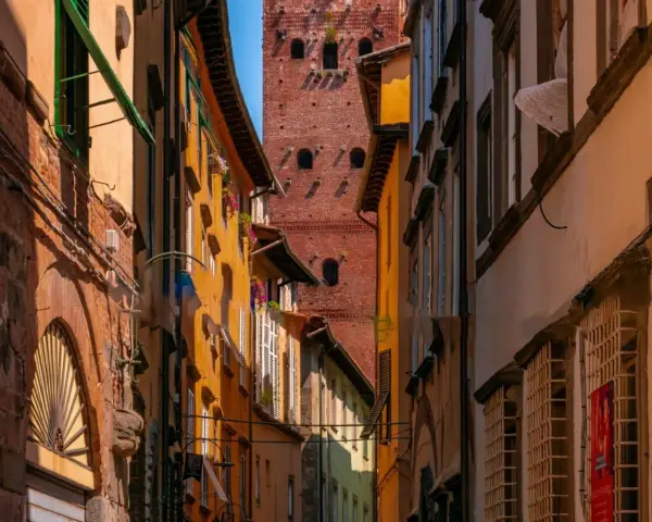 Un vicolo stretto a Lucca con edifici colorati e la torre Guinigi che svetta in lontananza.