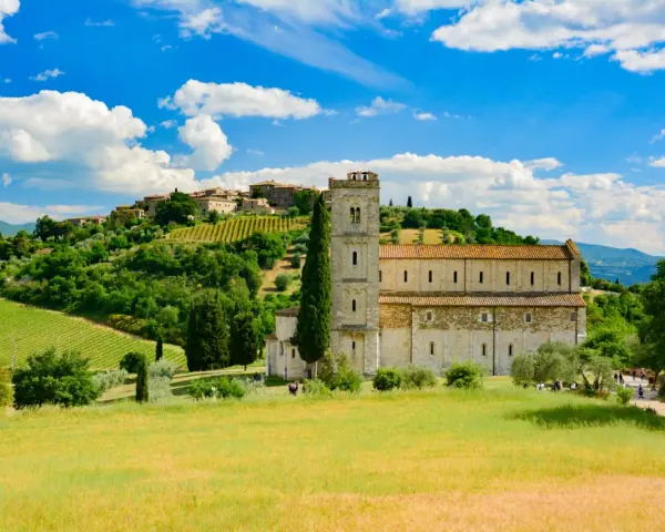 Abbazia di Sant'Antimo, un gioiello romanico immerso nel verde della Toscana, con vigneti e un borgo sullo sfondo.