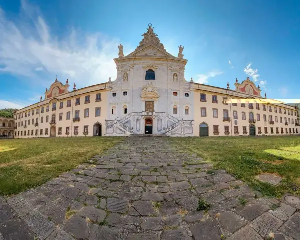 La maestosa Certosa di Calci si erge sotto un cielo azzurro, con un sentiero di pietra che conduce alla sua imponente facciata.