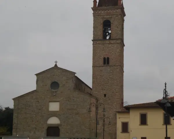 La chiesa di Sant'Agostino ad Arezzo, con il suo imponente campanile in pietra, si staglia contro un cielo nuvoloso.