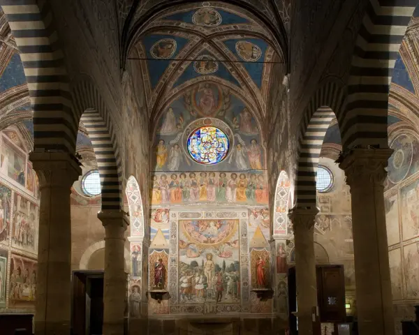 Interno del duomo di San Gimignano, con affreschi medievali che narrano storie sacre, volte a crociera a strisce bianche e nere e un rosone colorato.
