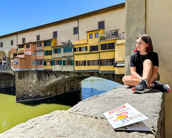 Ragazza con capelli rosa seduta sul Ponte Vecchio a Firenze, con una guida per bambini in primo piano.