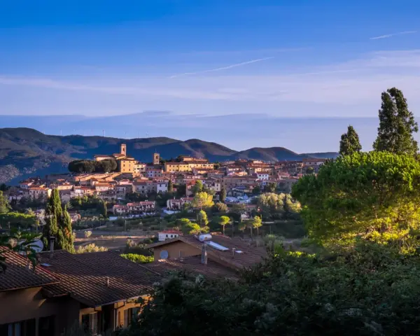 Panoramica di Montescudaio cosa vedere: borgo toscano con case in pietra, chiese e torri, immerso nel verde collinare sotto un cielo azzurro.