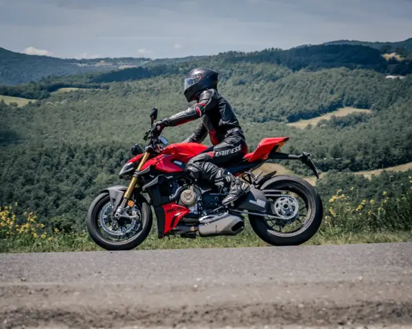 Motociclista in tuta rossa e nera sfreccia su una Ducati rossa lungo il passo del giogo, tra colline verdi e cielo azzurro.