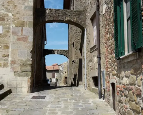 Un vicolo suggestivo a Vetulonia, tra antiche mura di pietra e archi che incorniciano il cielo azzurro. Scopri cosa vedere in questo borgo storico.