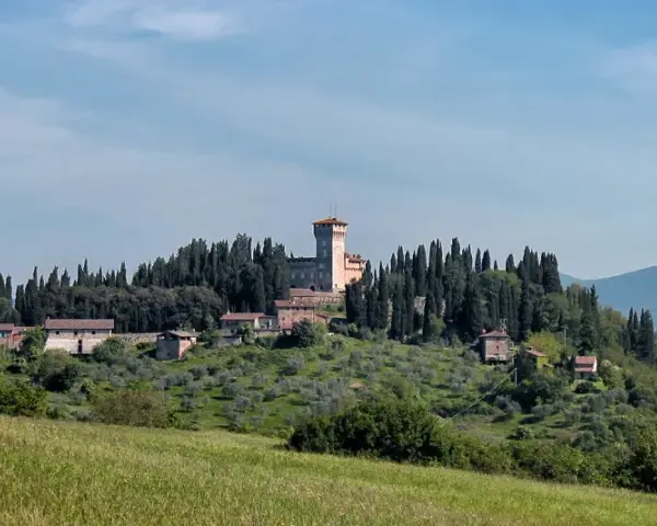 Un borgo collinare con un castello domina il paesaggio toscano di Scarperia e San Piero, circondato da cipressi e ulivi.