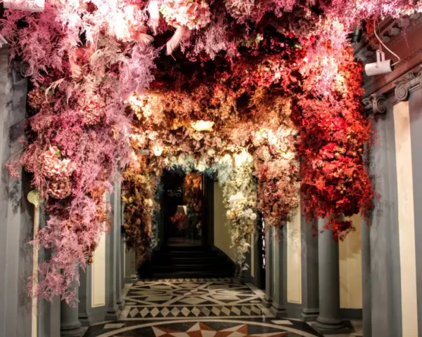 Ingresso fiorito, un arco di fiori rossi e rosa che ricorda l'antica farmacia di Firenze.