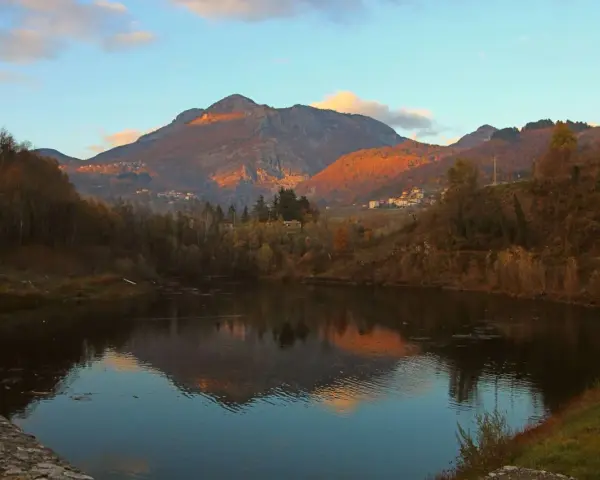 Tramonto dorato sulle montagne vicino a Villa Collemandina, con un lago che riflette il paesaggio autunnale.
