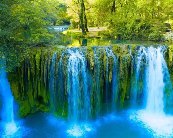 Cascata rigogliosa nel Val d'Arno, con acqua azzurra che scende su rocce ricoperte di muschio verde.