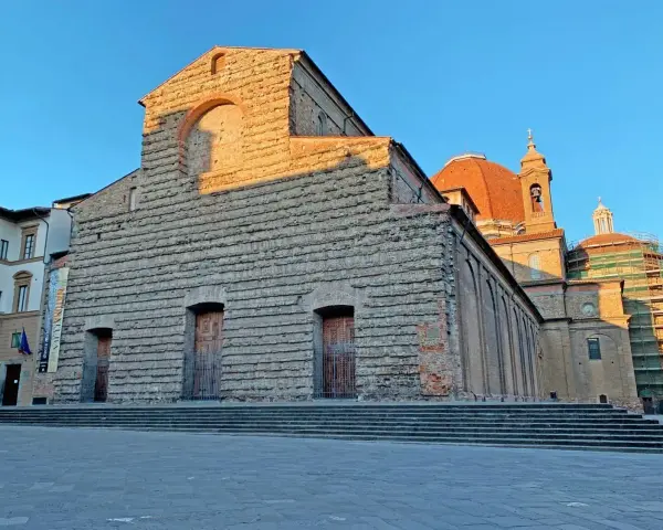 La facciata in pietra di San Lorenzo a Firenze, con la cupola arancione che domina il cielo azzurro.