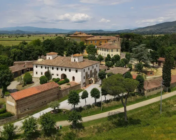 La Tenuta Frassineto, un complesso di edifici storici immerso nel verde, con campi coltivati e colline sullo sfondo.