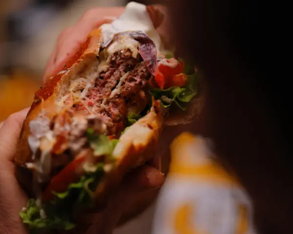 Mani che stringono un succulento hamburger, un'esplosione di sapori tipica dello street food ad Arezzo.
