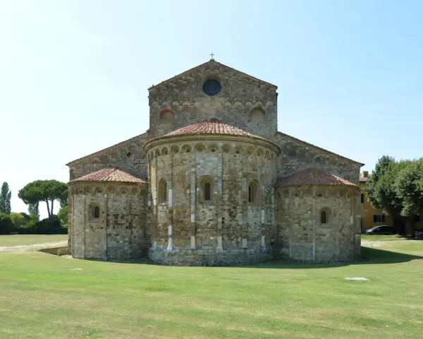 La Basilica di San Piero a Grado, con le sue absidi romaniche e il prato verde circostante, si staglia contro un cielo limpido.