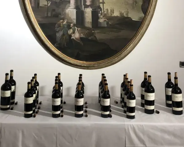 Bottiglie di vino Oreno della Tenuta Setteponti disposte su un tavolo, con un dipinto ovale sullo sfondo.