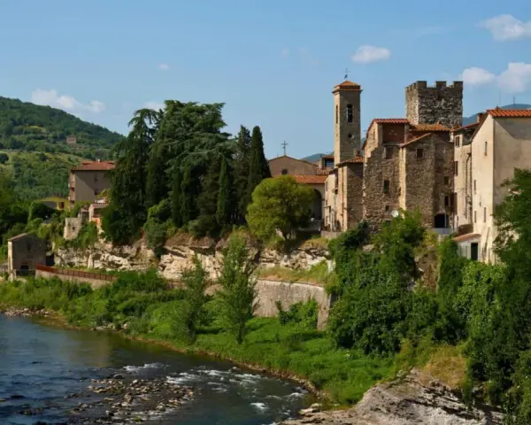 Borgo medievale di Subbiano, Arezzo, con il fiume che scorre ai suoi piedi e il verde rigoglioso che abbraccia le antiche pietre.