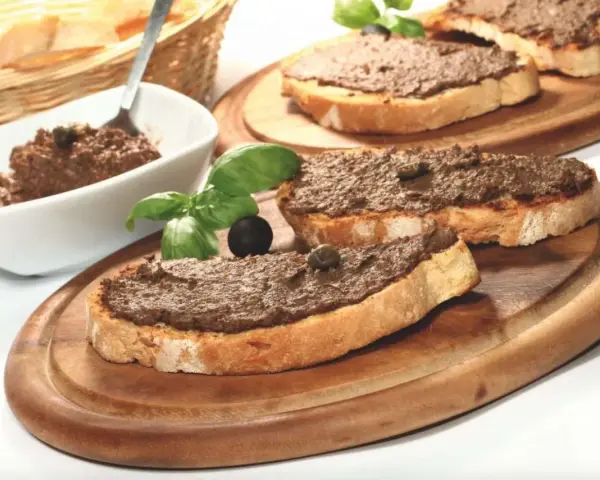 Toasted bread slices topped with dark spread, garnished with basil, olives, and capers.