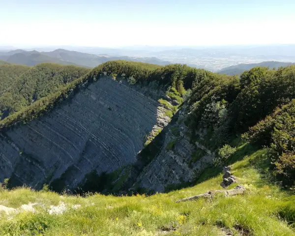 Panoramica mozzafiato sull'Alpe della Luna, con rocce stratificate che si ergono tra boschi rigogliosi e un cielo azzurro.