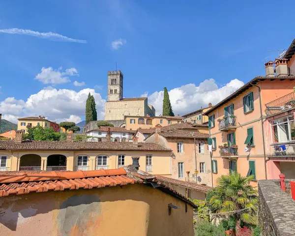 Panoramica di Barga, Lucca, con case colorate e il Duomo in cima alla collina sotto un cielo azzurro con nuvole bianche.