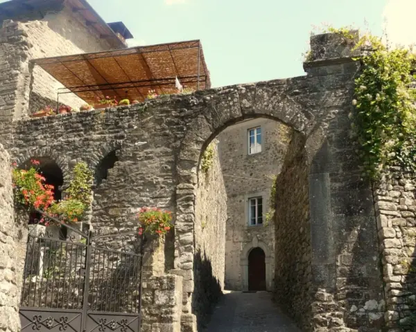 Un vicolo antico a Casola in Lunigiana, con un arco in pietra, mura di sassi e fiori rossi che sbocciano.