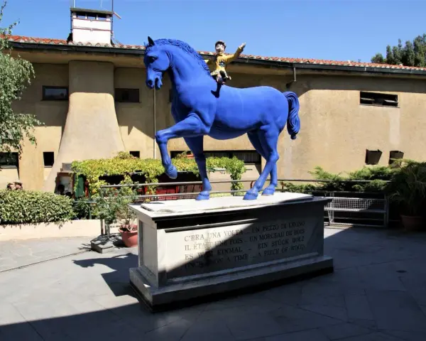 Un cavallo blu con Pinocchio a cavalcioni, simbolo del paese di Collodi. La statua è posta su un piedistallo con la frase "C'era una volta... un pezzo di legno" in più lingue.