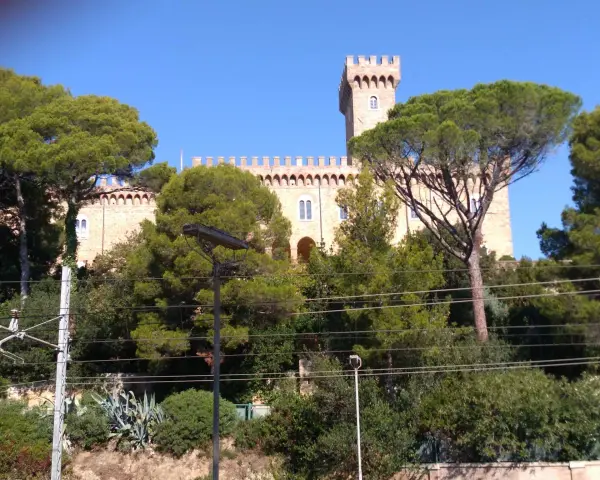Il Castello Pasquini, con la sua torre imponente, emerge tra alberi verdi e un cielo azzurro.