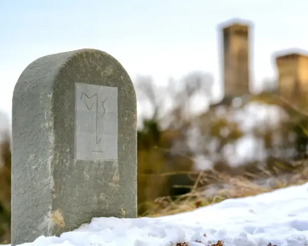 Monumento in pietra con simbolo inciso, sulla via Matildica del Volto Santo. In lontananza, castelli innevati.