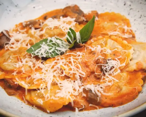 Tordelli versiliesi in un piatto bianco, conditi con sugo rosso, funghi, parmigiano grattugiato e basilico fresco.