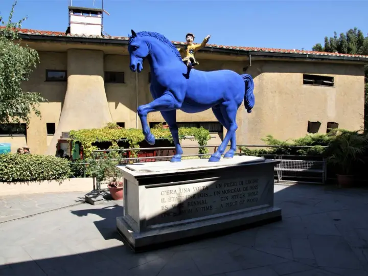 Un cavallo blu con Pinocchio a cavalcioni, simbolo del paese di Collodi. La statua è posta su un piedistallo con la frase "C'era una volta... un pezzo di legno" in più lingue.